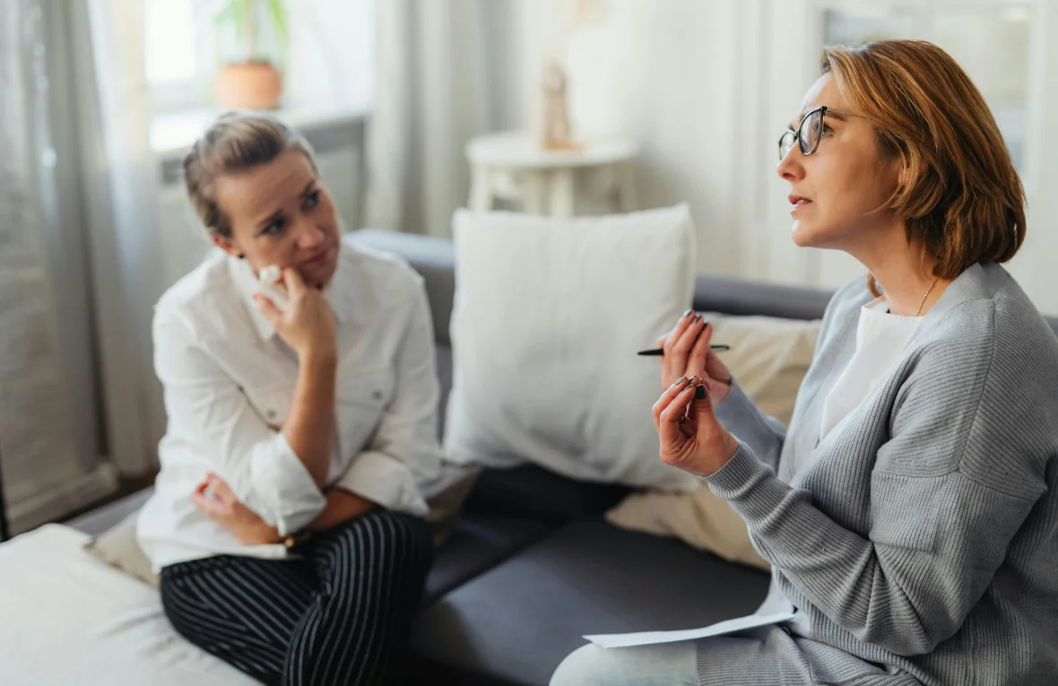 Two women sitting together in a therapy session, with one speaking and the other listening closely, symbolizing Cognitive Behavioral Therapy (CBT) in Tempe AZ.