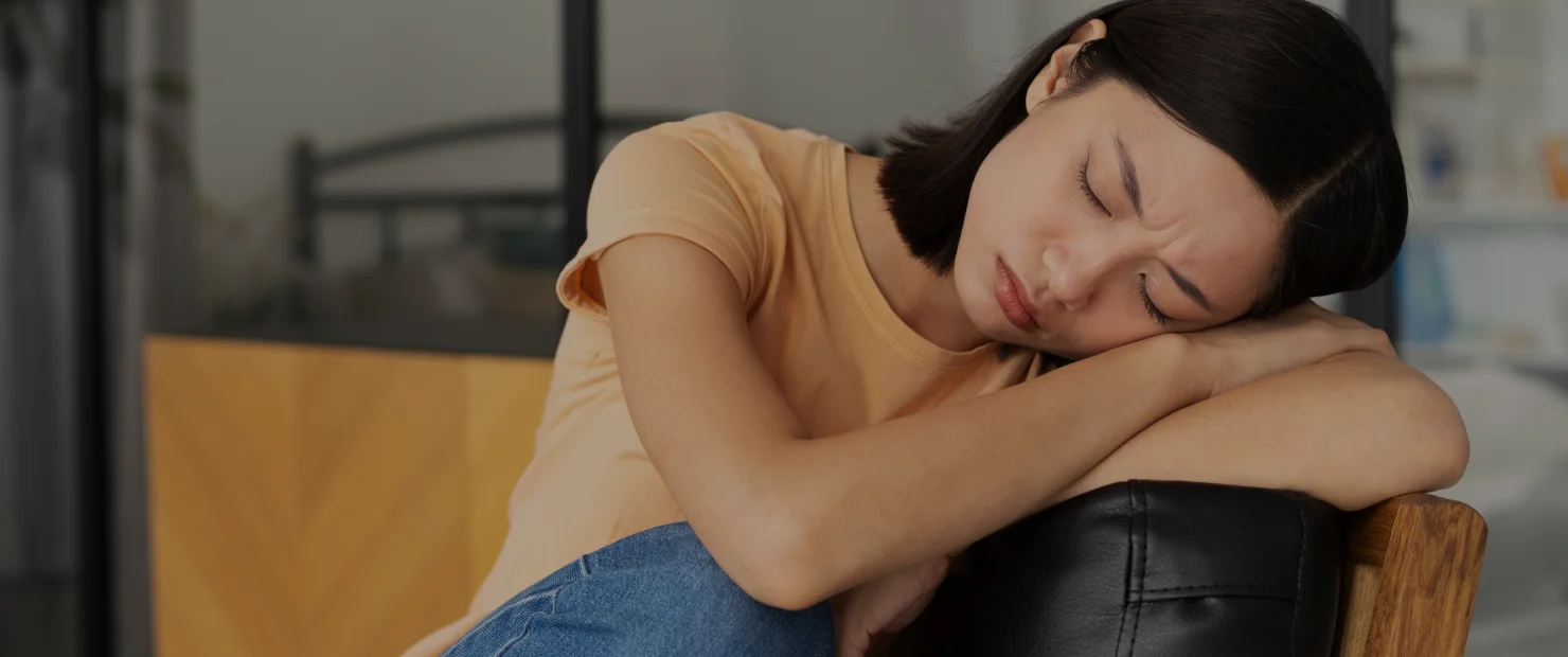Young woman sitting with head resting on her arms and eyes closed, symbolizing emotional stress and the healing focus of Brainspotting Therapy in Tempe AZ.